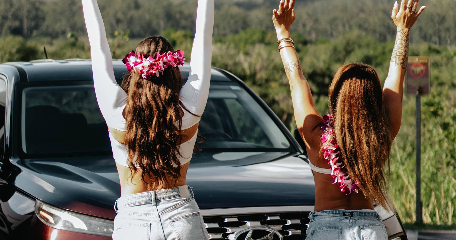 Two travelers wearing orchid leis beside their Makoa rental SUV at a Maui valley lookout